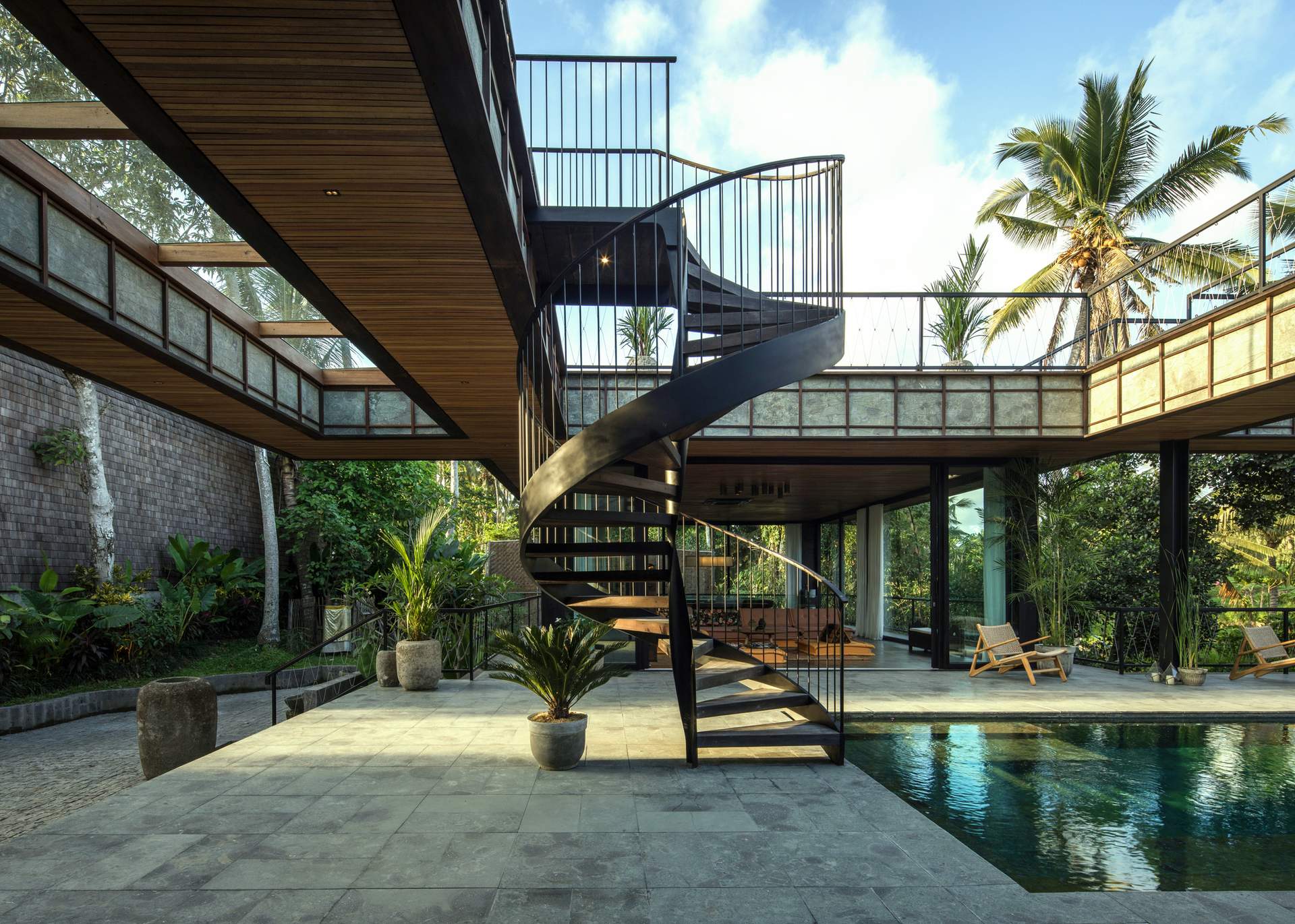 Modern tropical villa with spiral staircase, pool, and lush greenery
