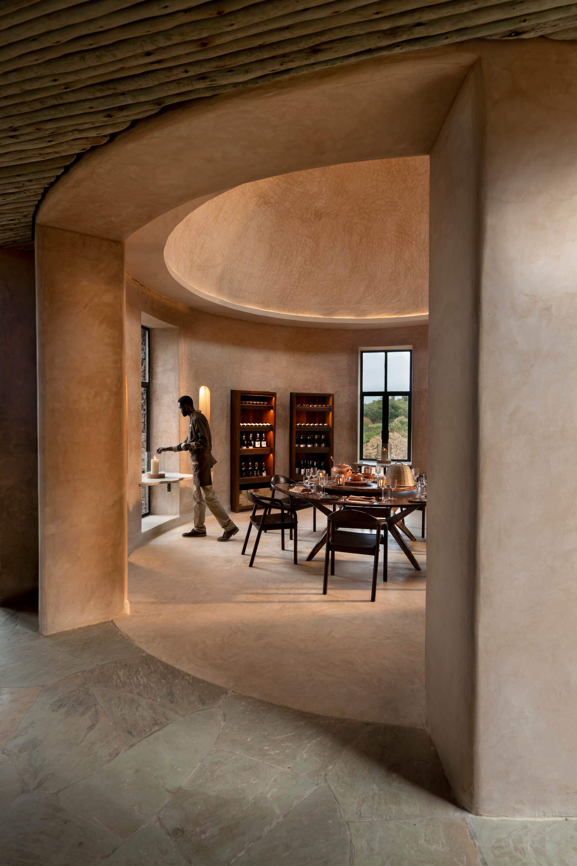 A man is standing in a room with a table full of wine bottles.