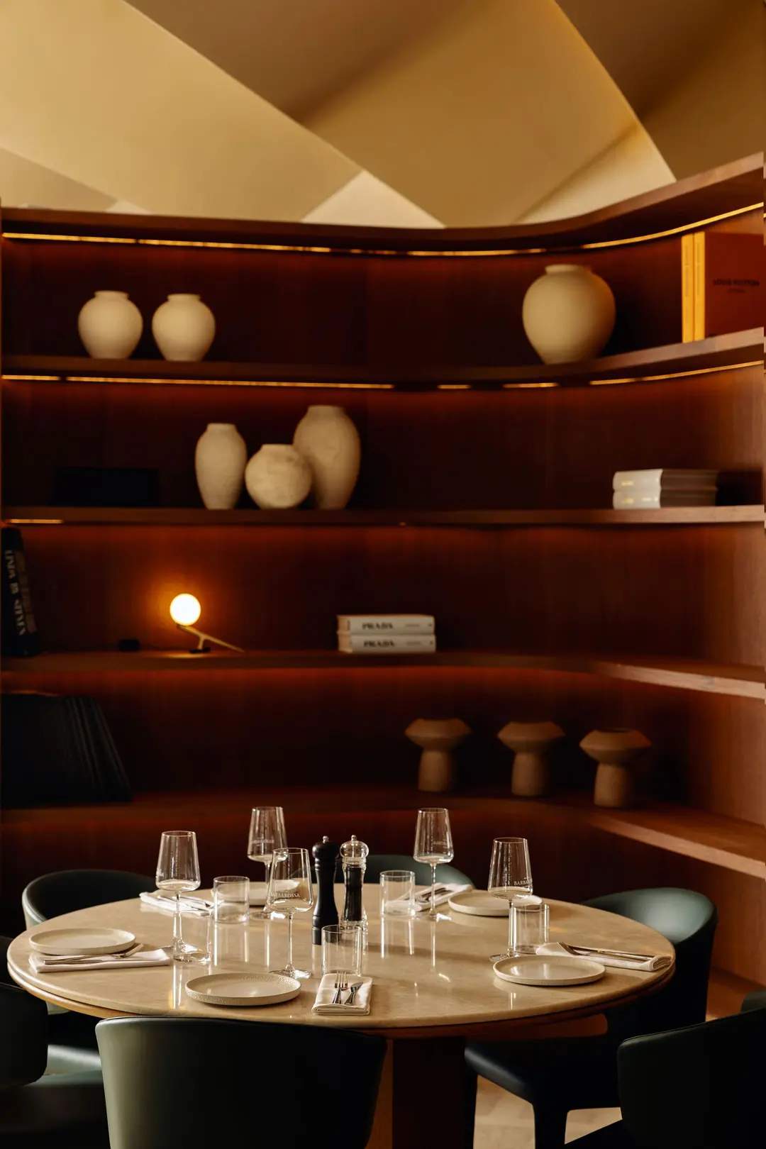 A table with wine glasses and a vase on a shelf above it.