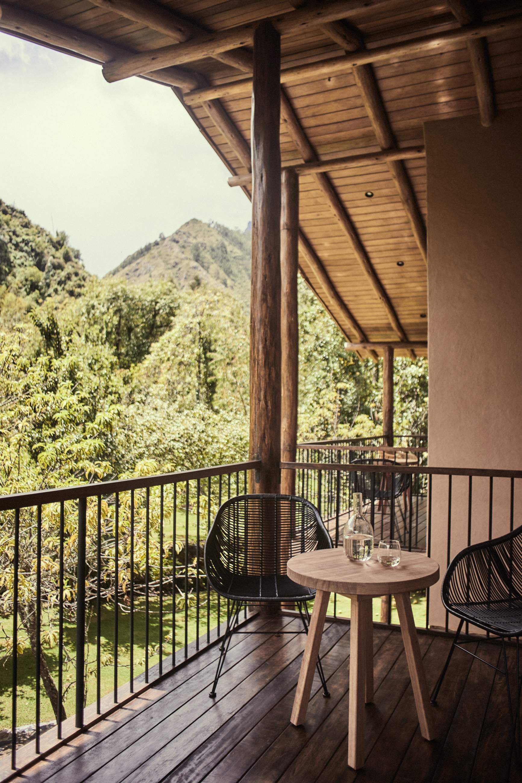A table with a glass of water on it sits on a deck overlooking a forest.