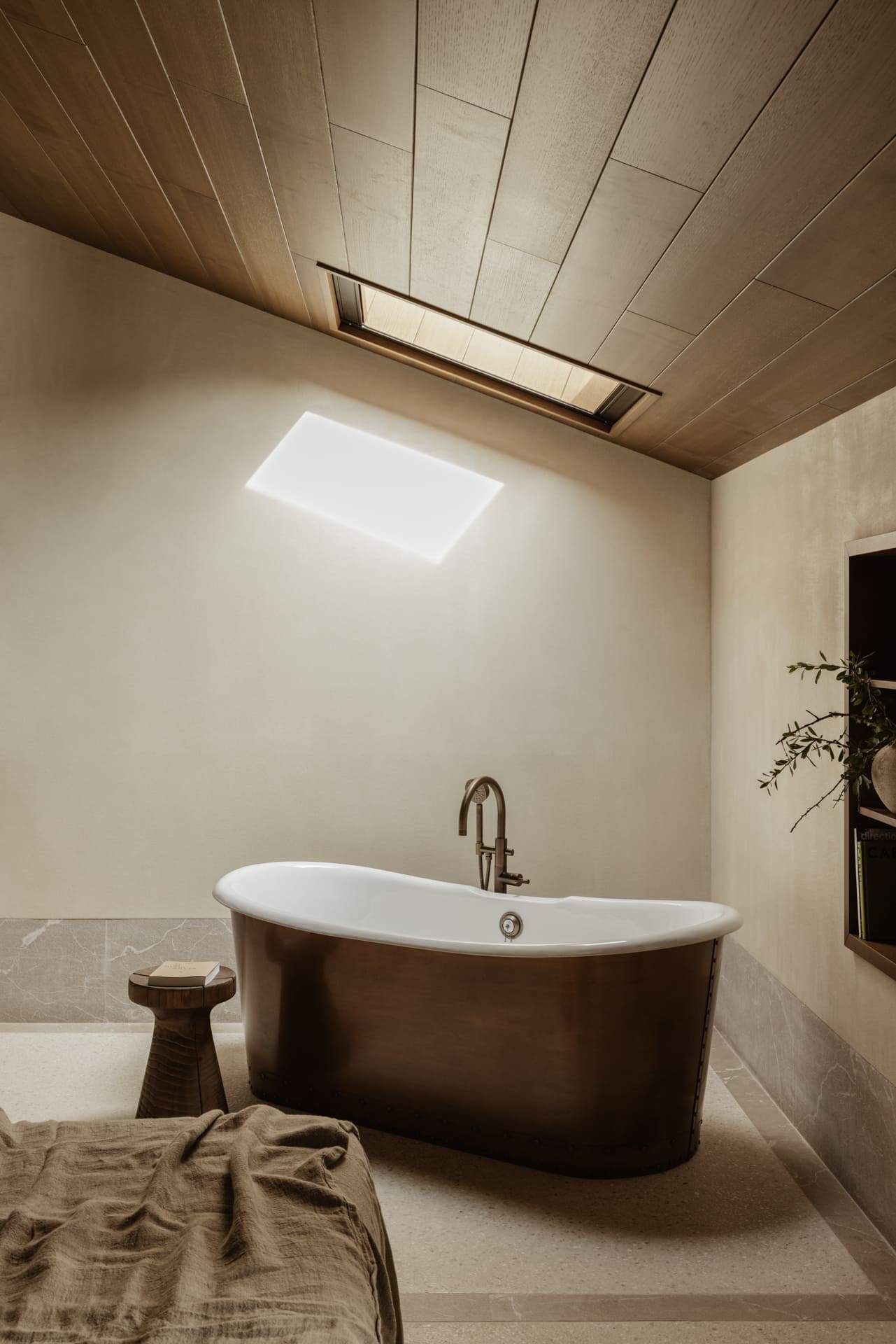 A brown bathtub with a wooden stool next to it.