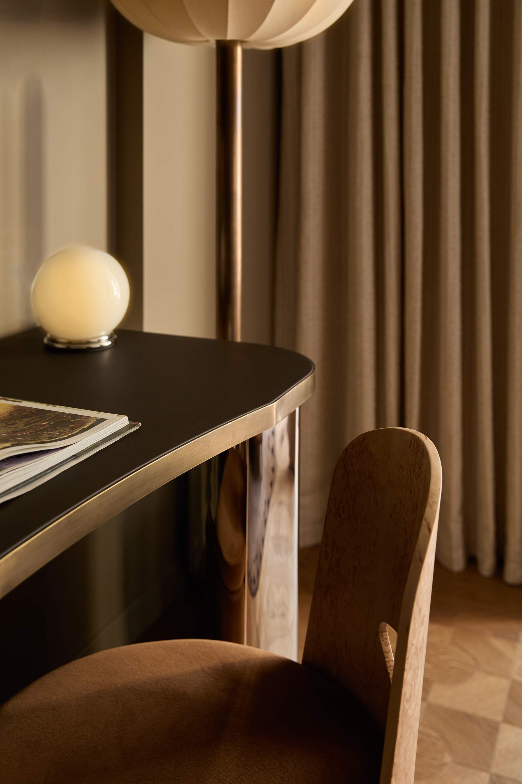A wooden chair is in front of a desk with a lamp and a magazine.