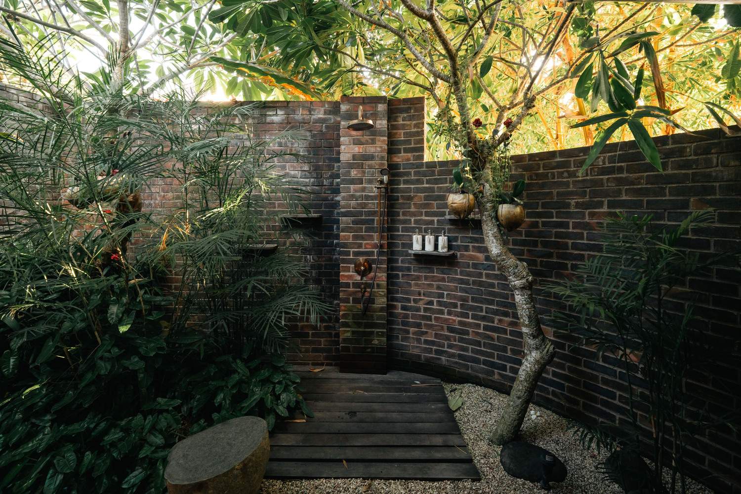 A wooden bench is in front of a brick wall with a shower head.