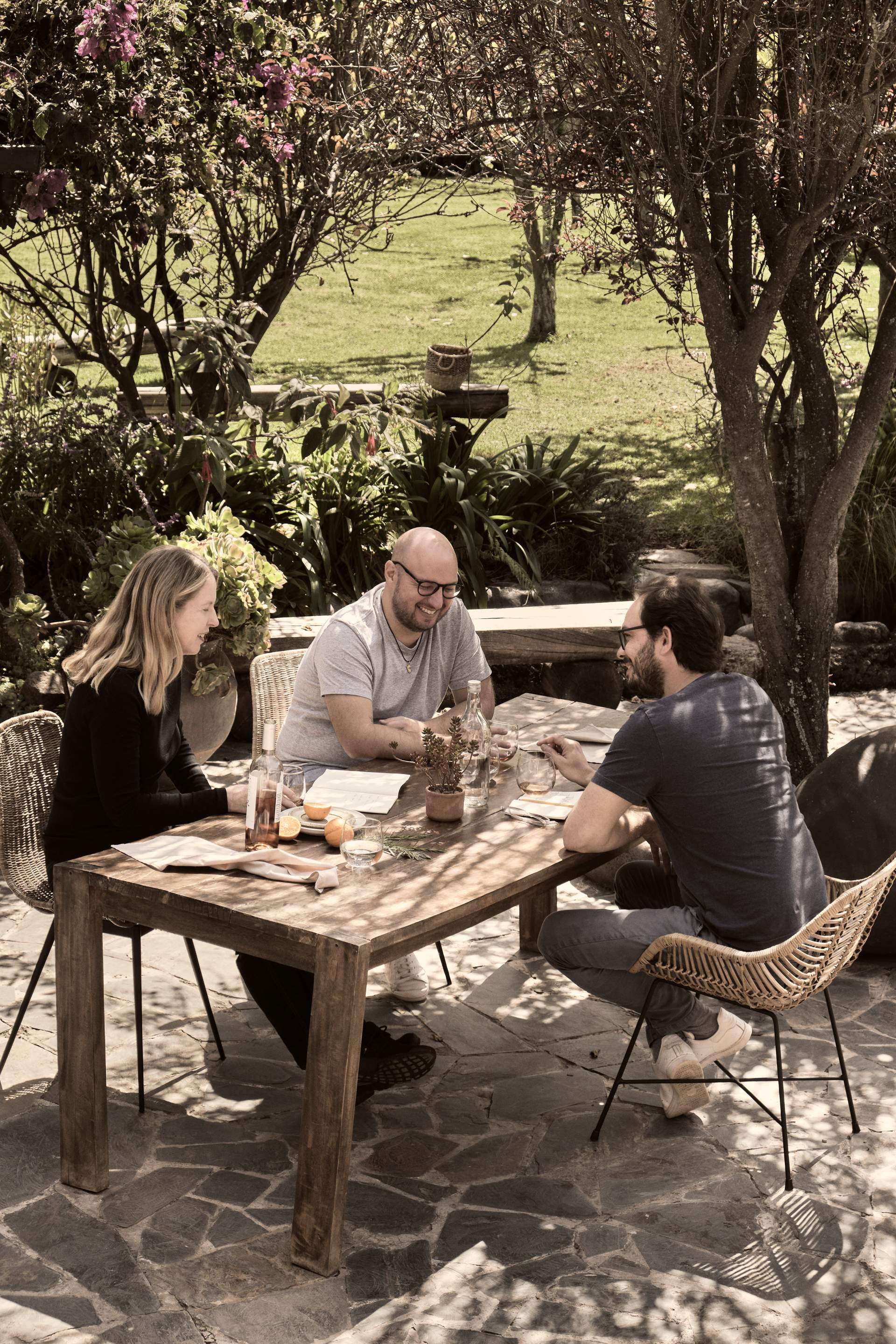 Three people sitting at a table with wine glasses and a bottle.