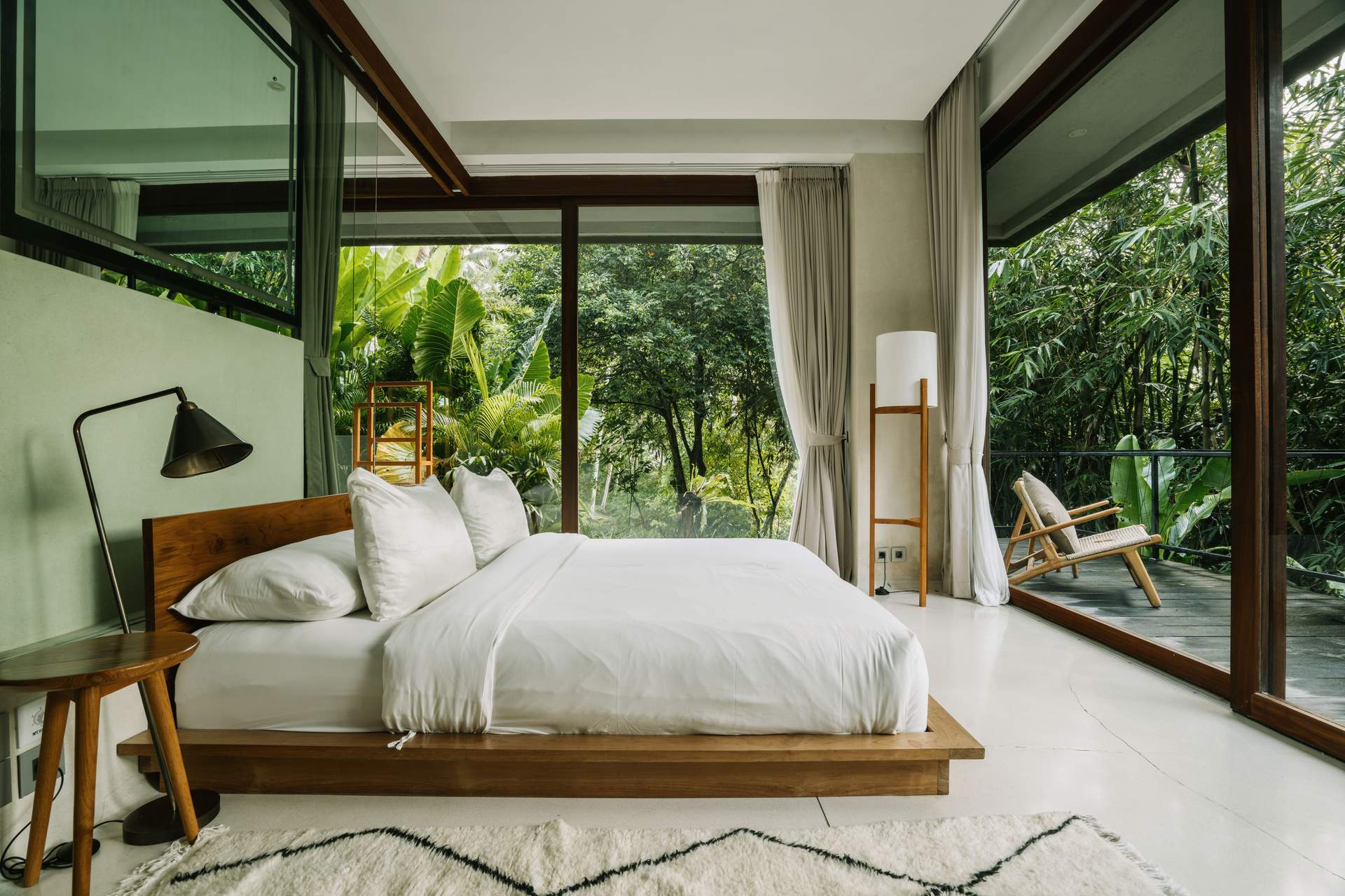 A bedroom with a white bed and a view of the forest.