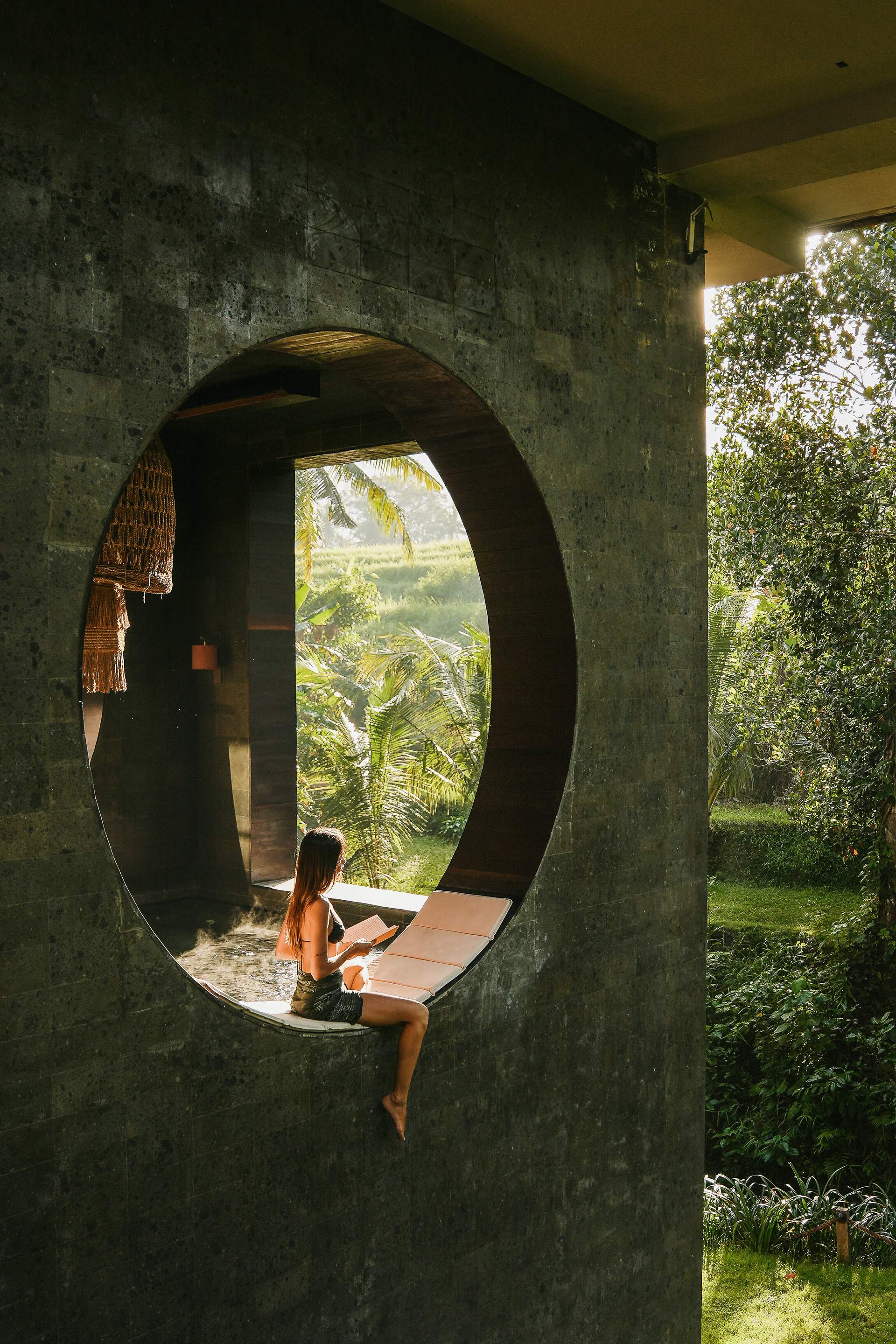 A woman sits in a round window overlooking a jungle.