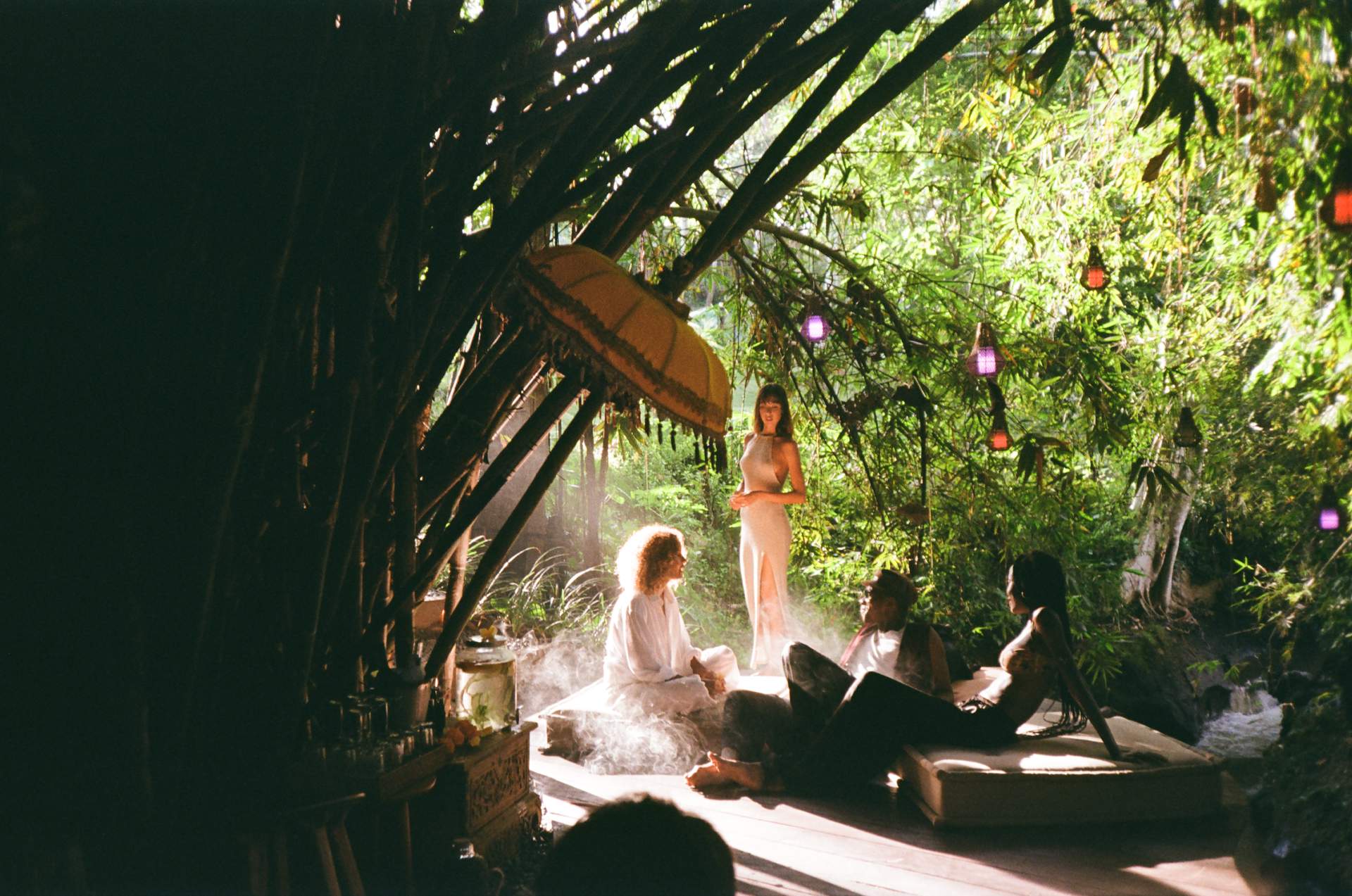A group of people sitting on a bed in a hut.