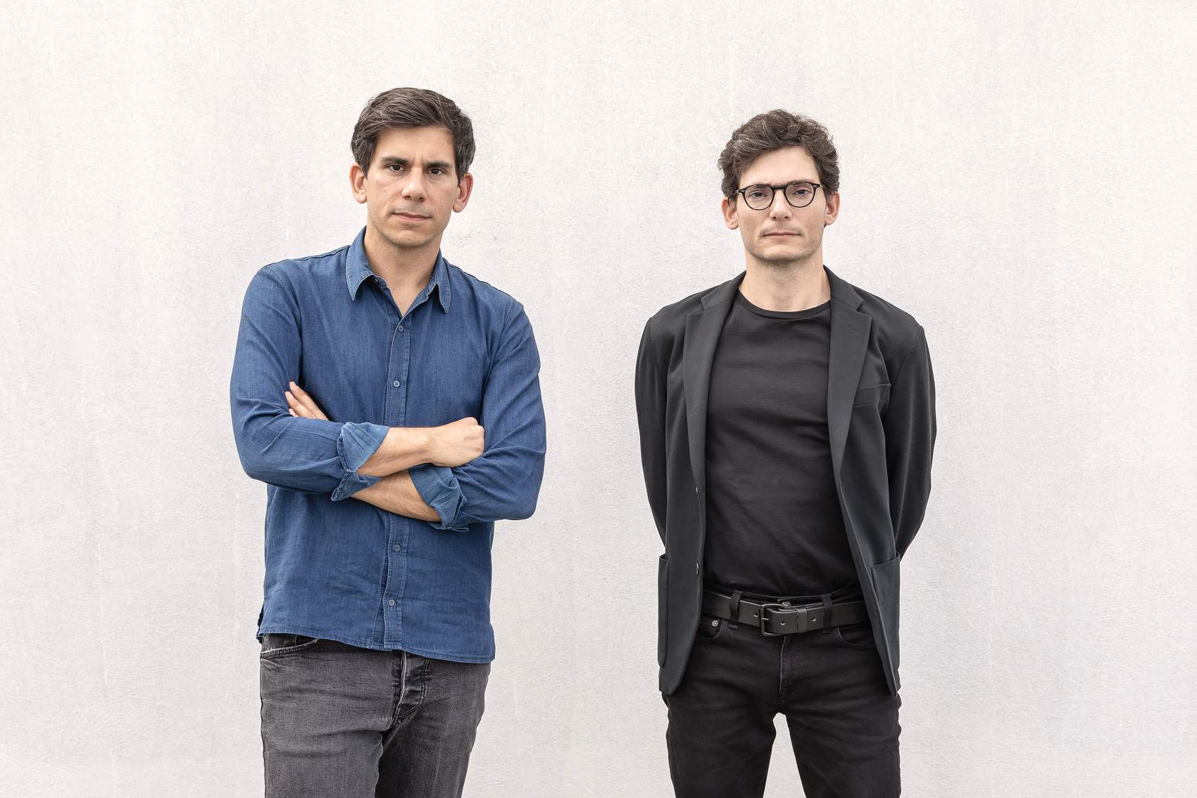 Two men wearing black jackets and glasses stand side by side.