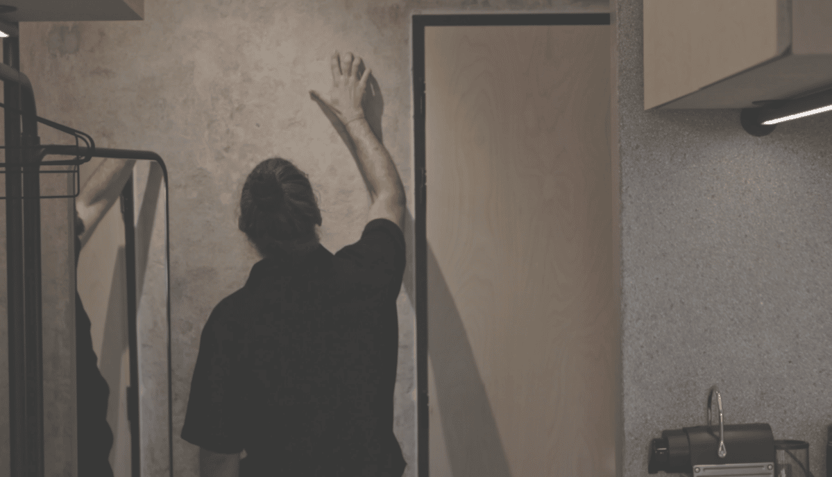 A man wearing a black shirt is touching a wall.