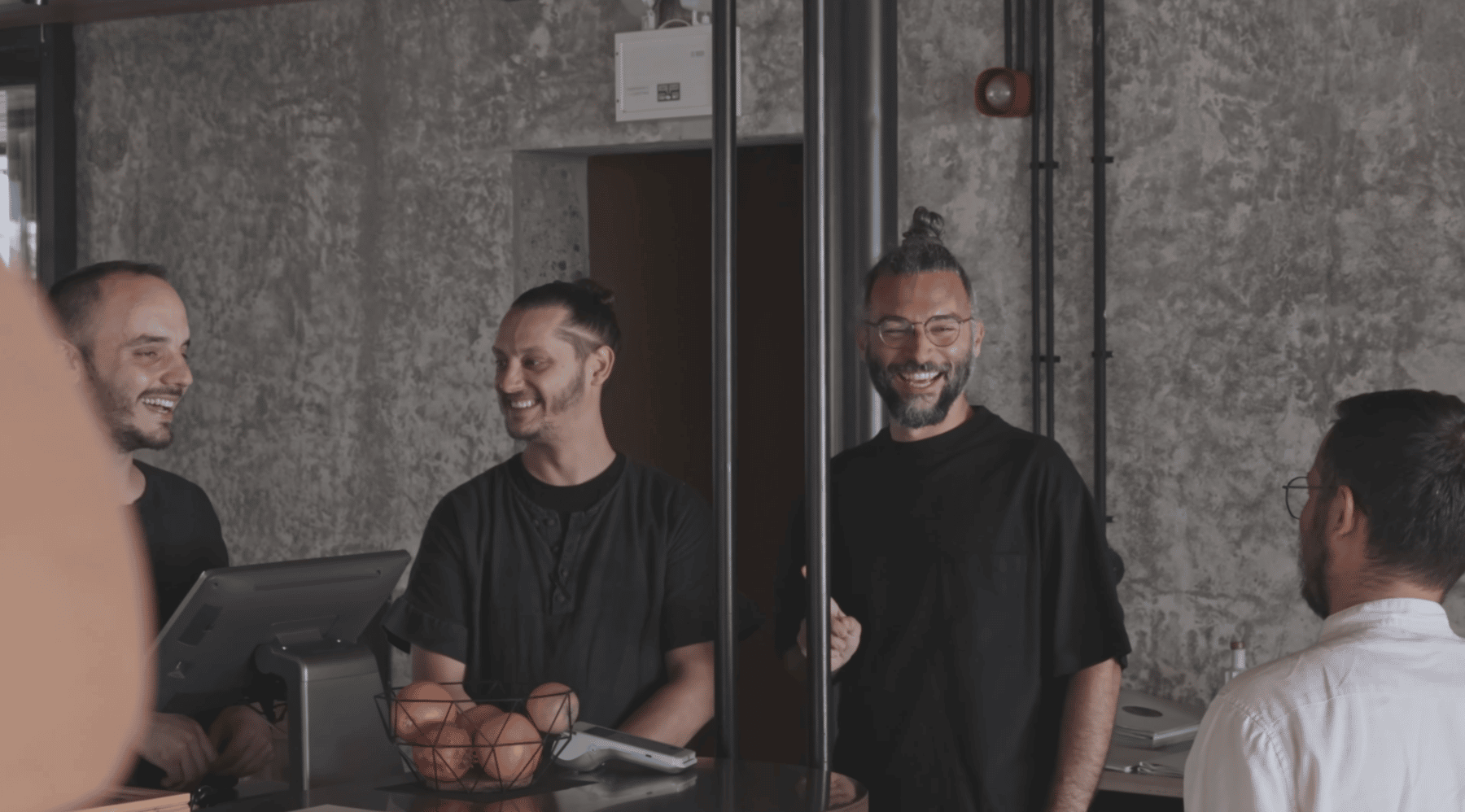 Two men standing in front of a counter with a basket of fruit.