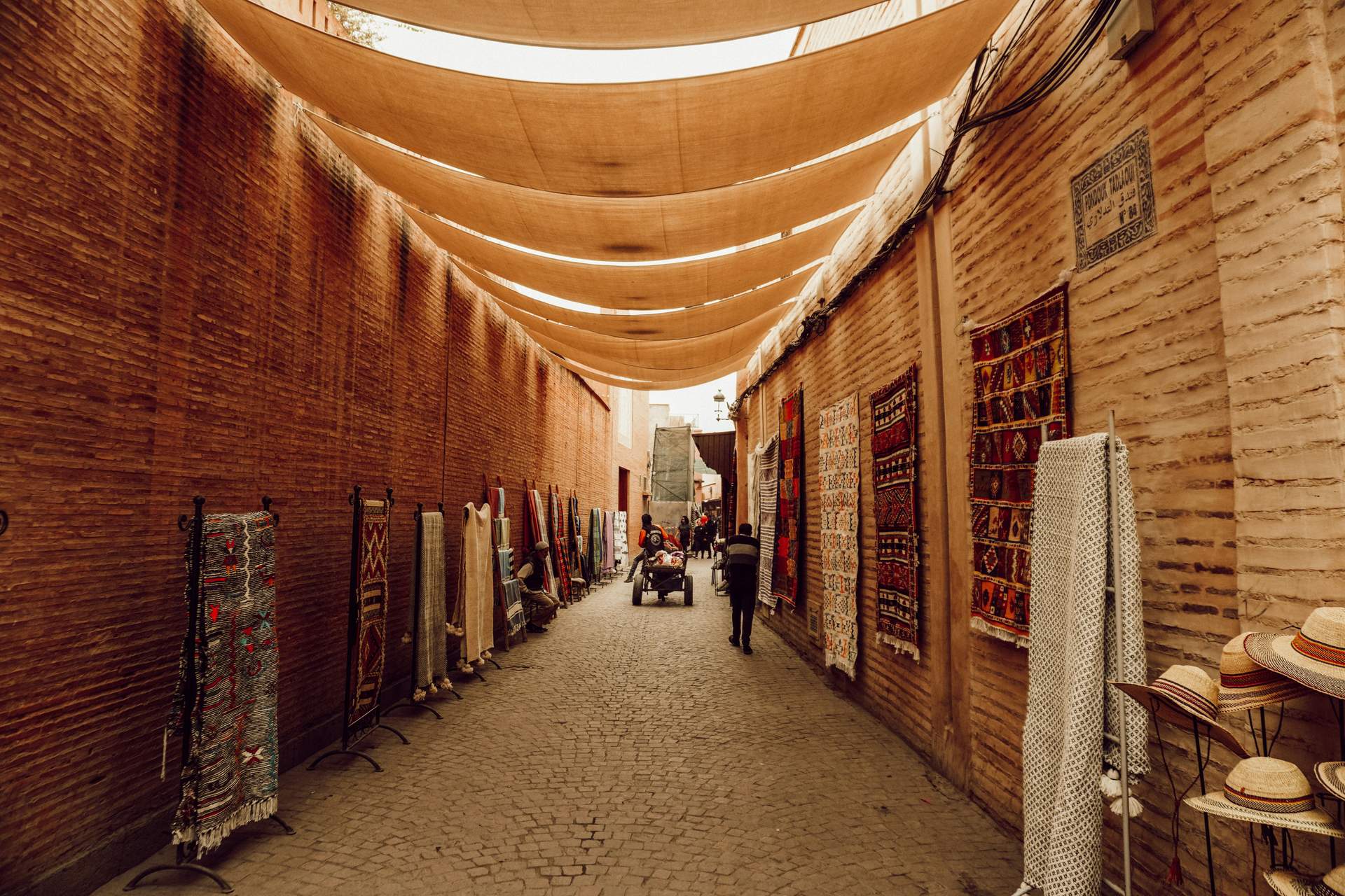 A narrow alleyway with a canopy of cloths and people walking.