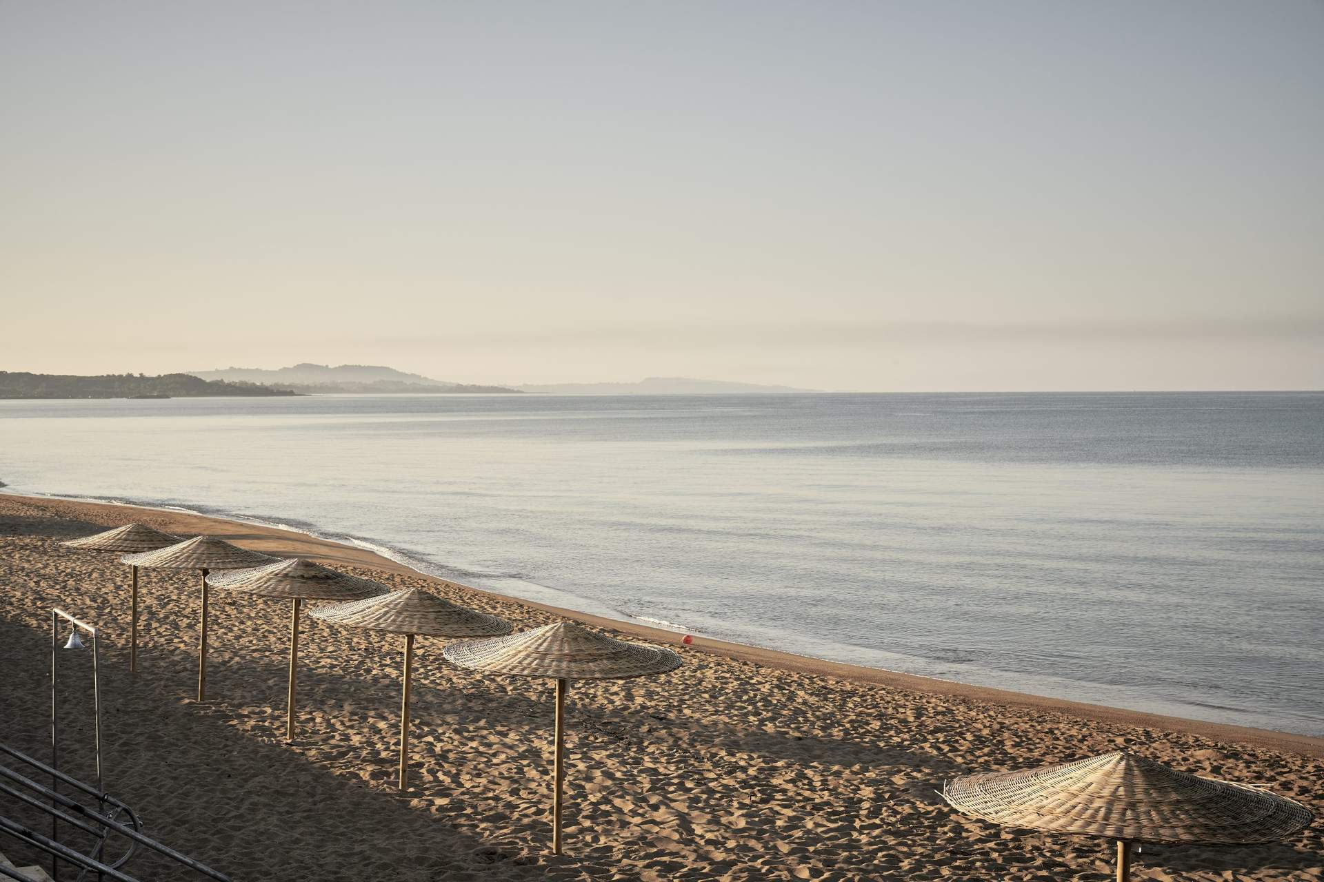 A beach with a few umbrellas and a person standing on the sand.
