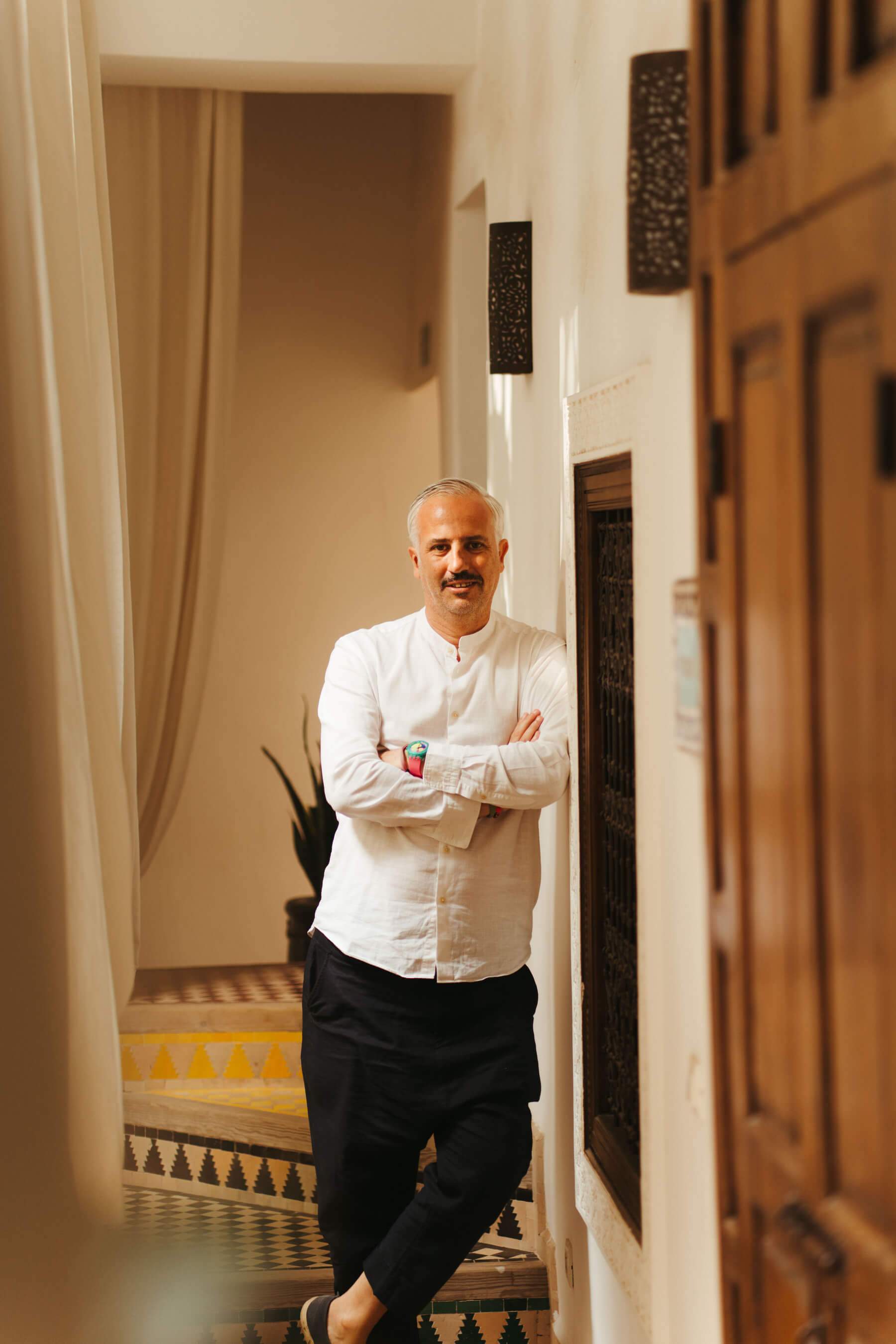 A man wearing a white shirt and black pants stands in a hallway.