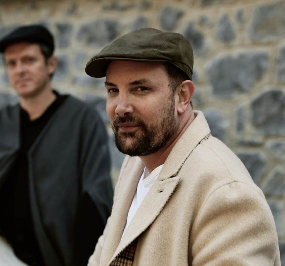 Two men wearing hats and jackets, one of them is wearing a brown hat.