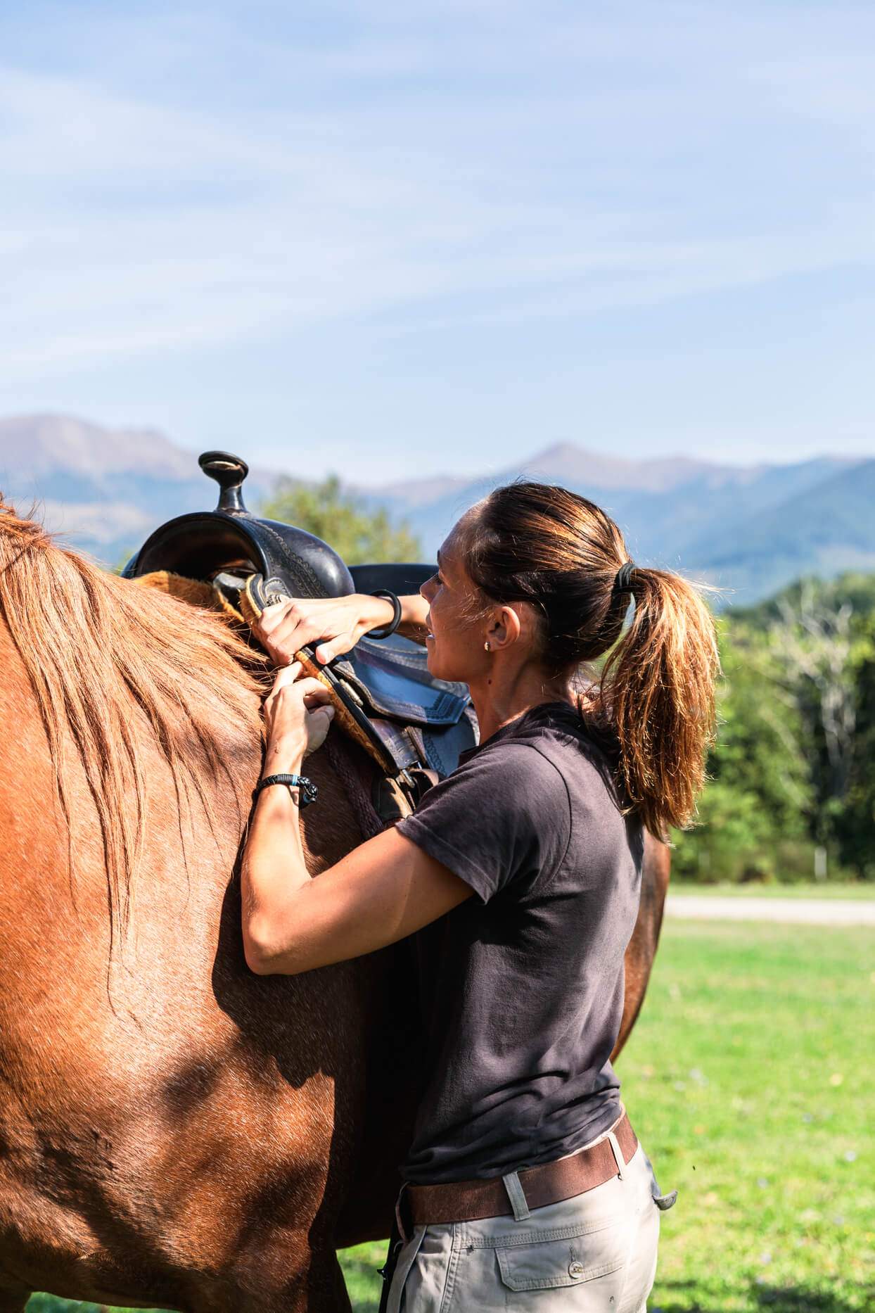 A woman is adjusting a horse's saddle.
