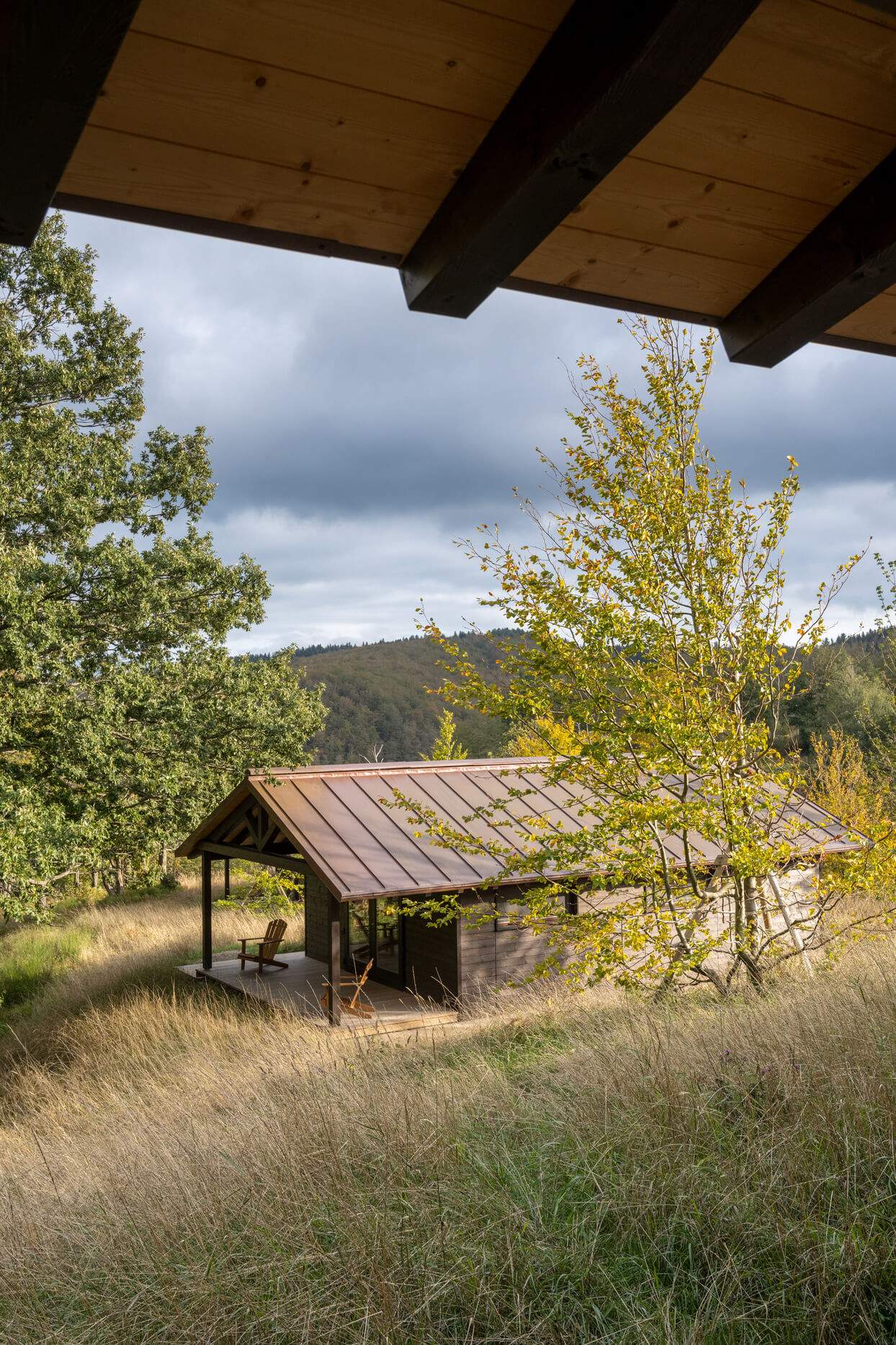 A small wooden house with a porch and a chair in front of it.