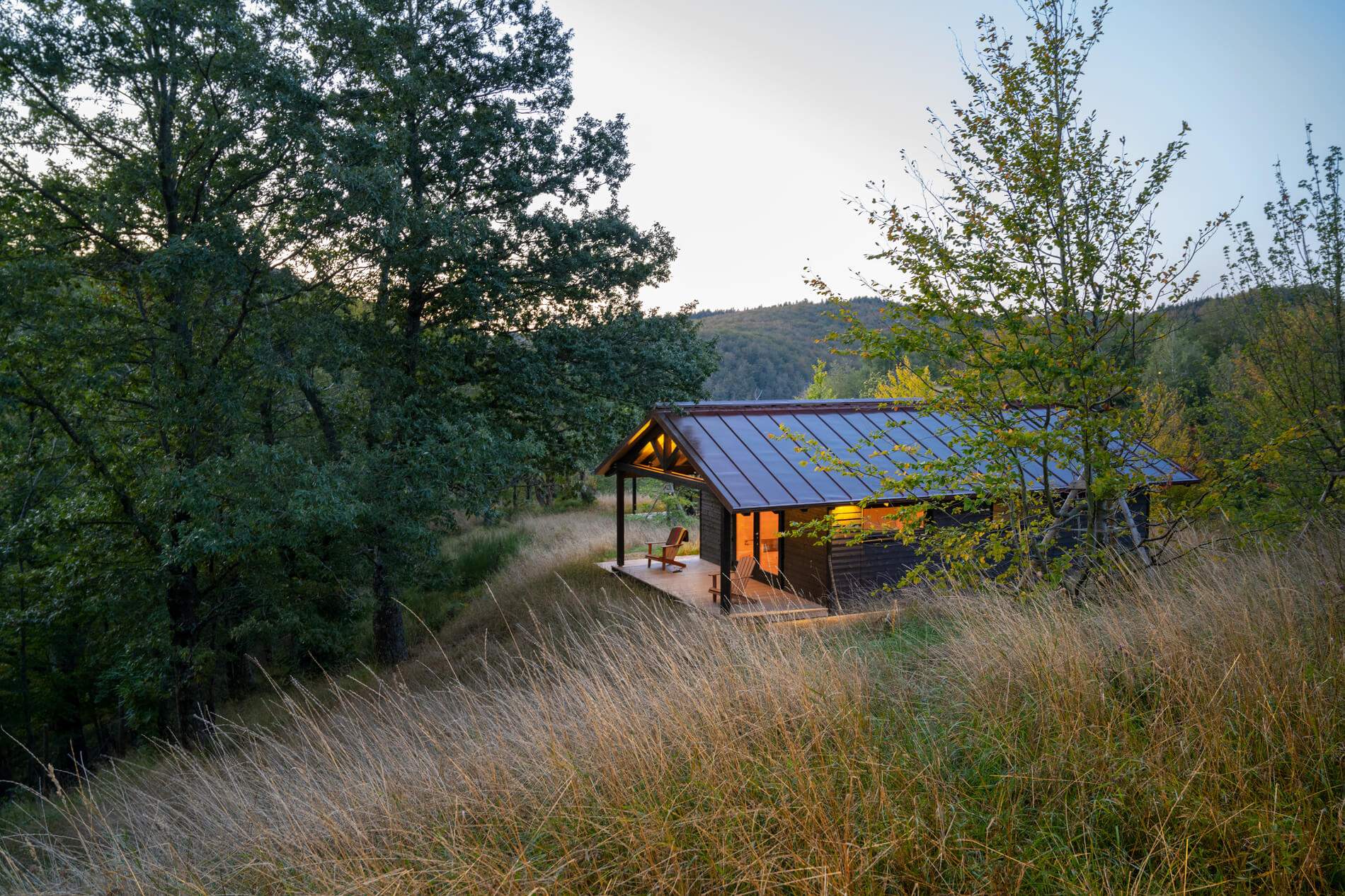 A cabin in the woods with a deck and a chair.