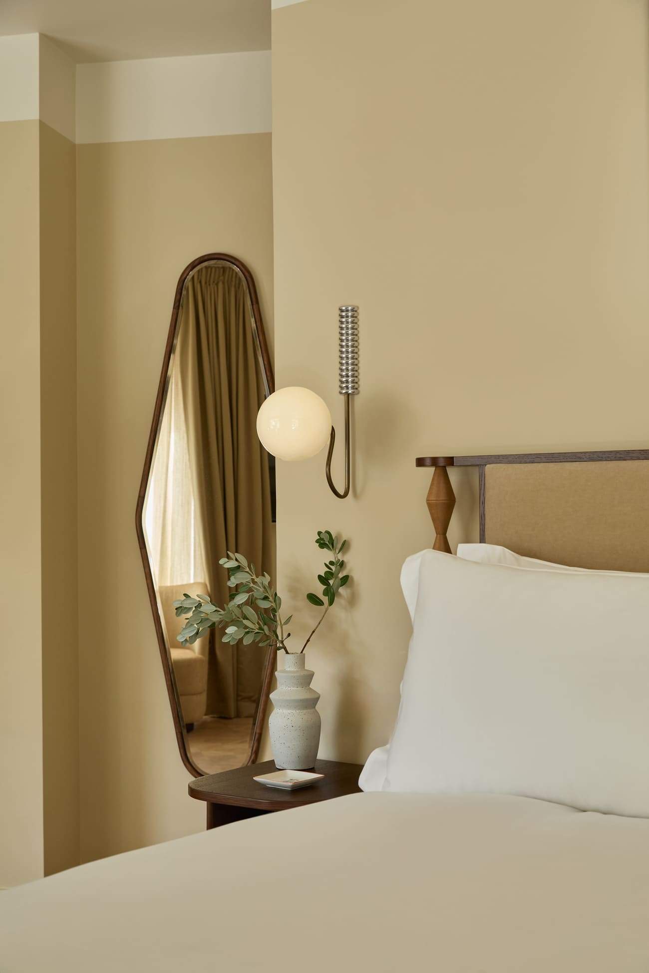 A bedroom with a bed, a mirror, and a lamp.