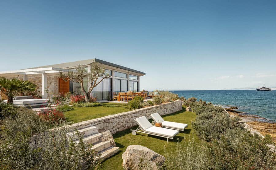 A white lounge chair sits on a grassy hillside overlooking the ocean.