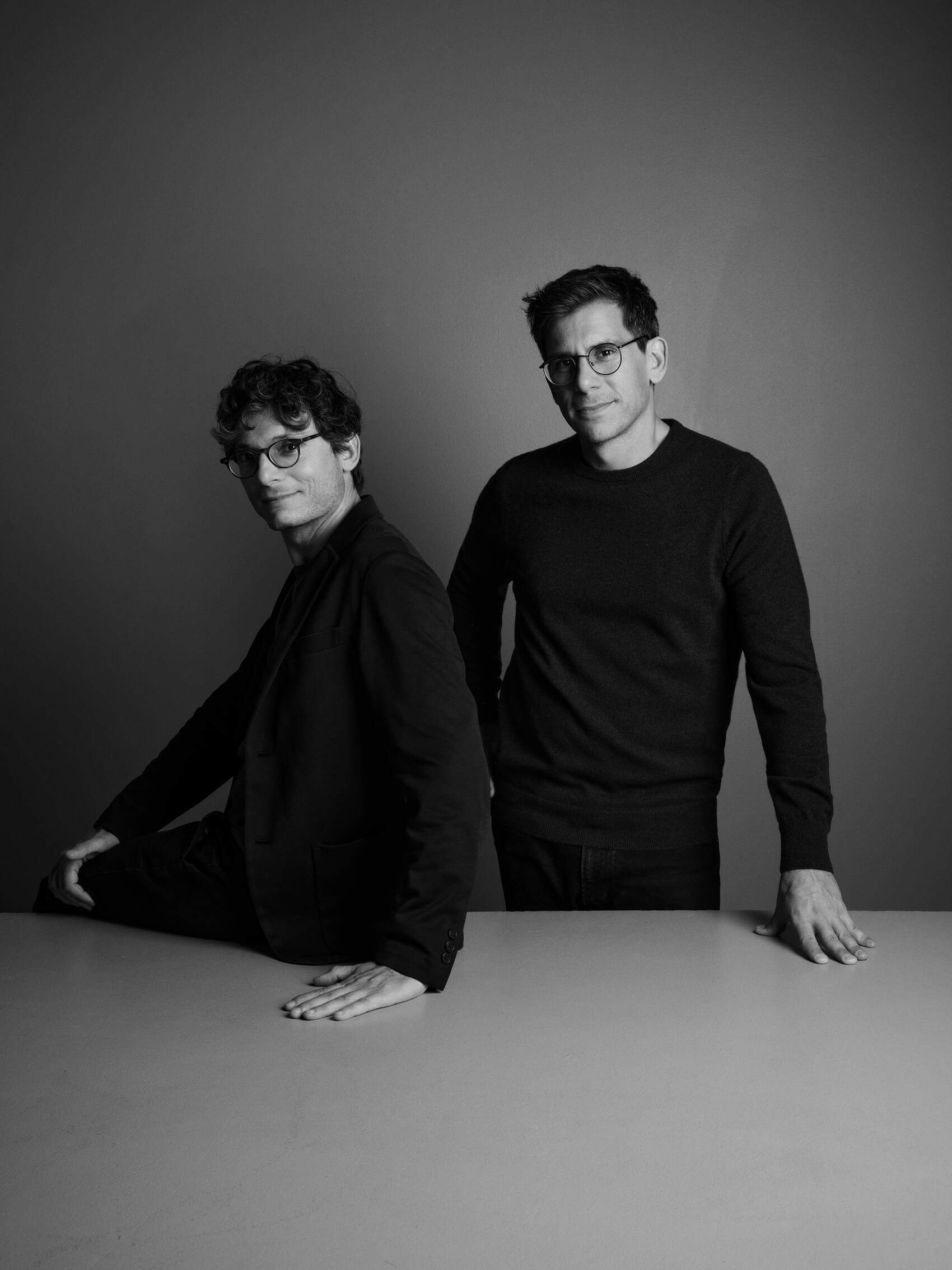 Two men wearing glasses and black shirts sitting at a table.