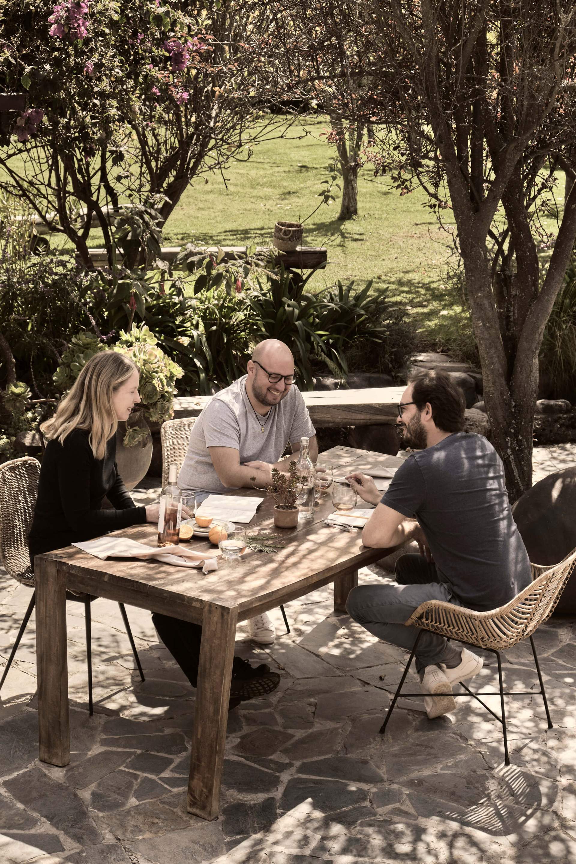 Three people sitting at a table in a garden.