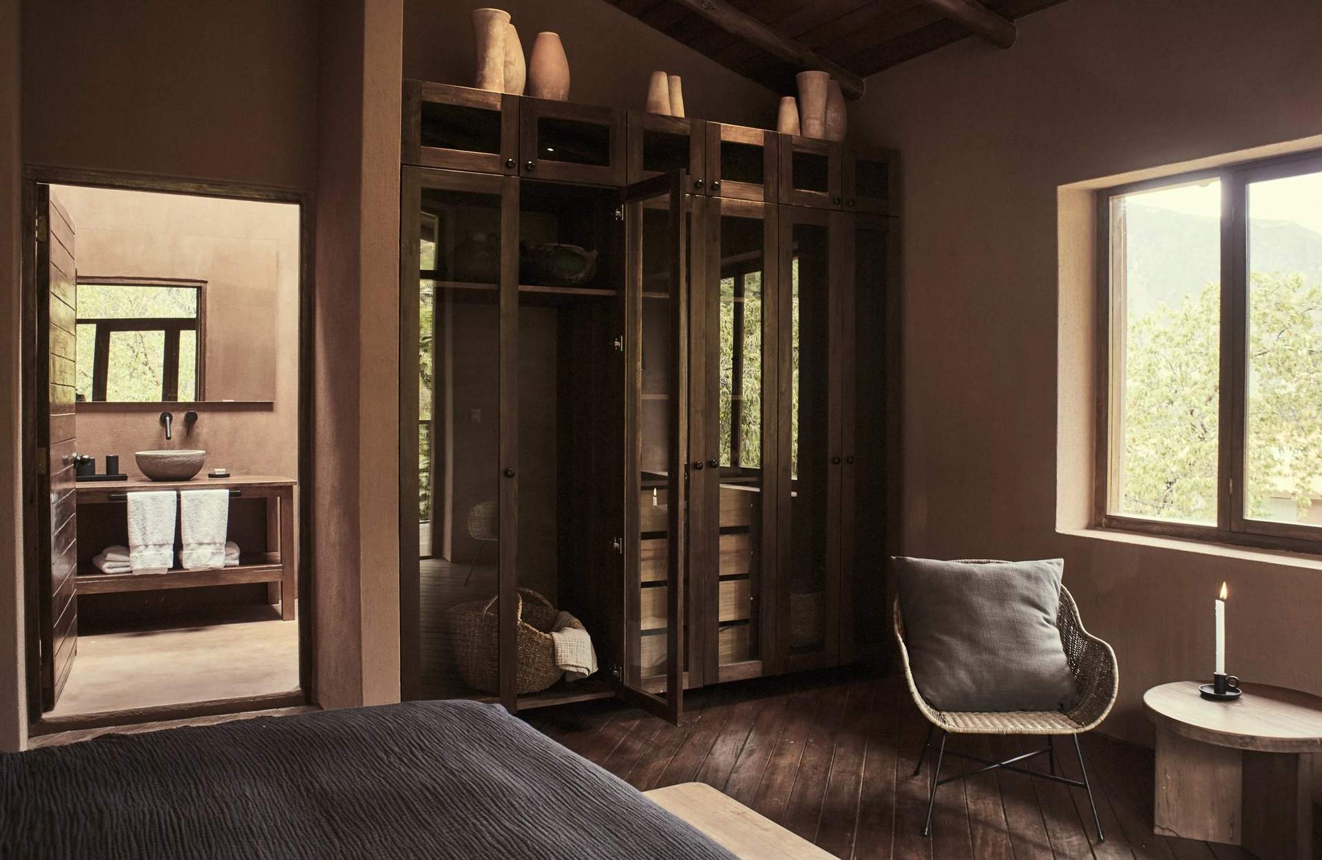 A bedroom with a bed, a chair, and a cabinet with a mirror.